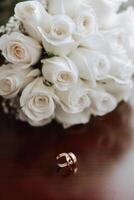 Wedding bouquet. White cut roses, green seed heads and leaves. Green stems and white ribbon and gold wedding rings. photo