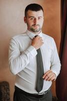 man in shirt dressing up and adjusting tie on neck at home. Wedding day concept,fashion, business, male style. photo