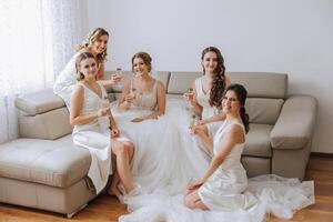 Photo bride with her friends drinking champagne from glasses. Cropped shot of a beautiful young bride and her bridesmaids having champagne before the wedding.