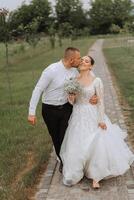 A handsome groom and an elegant bride in a lush white dress are walking in a summer park. Happy bride and groom getting ready for their best day. photo