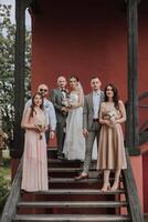 Groom and bride with friends pose on wooden stairs. A beautiful and elegant dress of the bride. Stylish wedding. Summer wedding in nature photo