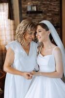 A beautiful and happy mother and her daughter, the bride, are standing next to each other. The best day for parents. Tender moments at the wedding. photo