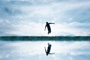 hombre saltando en el campo y reflejando en el lago foto