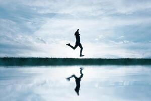 man jumping in the field and reflecting in the lake photo