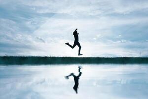 man jumping in the field and reflecting in the lake photo