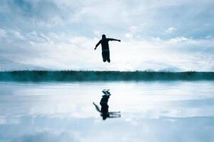 hombre saltando en el campo y reflejando en el lago foto