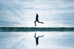 man jumping in the field and reflecting in the lake photo