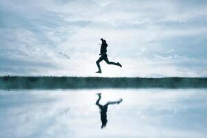 man jumping in the field and reflecting in the lake photo