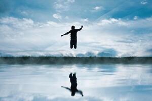 hombre saltando en el campo y reflejando en el lago foto