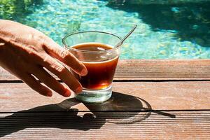 mujer Bebiendo café en el nadando piscina. Mañana café a junto a la piscina foto