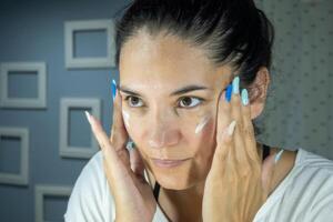 Cream smear. Beauty close up portrait of young woman with a healthy skin is applying a facial skincare product. Daily care routine of latin woman. Woman in front of the mirror. photo