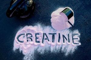 Strawberry creatine powder on a dark table with the word creatine written on it. This composition is accompanied by a scoop and a kettlebell. photo