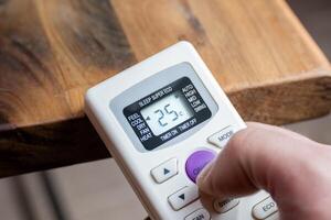 A man's hand holding the control of an air conditioner that marks the number twenty-five. photo