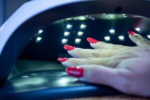 Young woman's hand using an ultraviolet lamp to dry her semi-permanent nails. Close up photo. photo