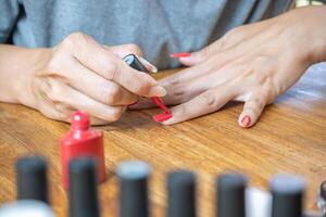 Hands of a young Latin woman painting her nails with a red polish on the table, surrounded by accessories for painting. photo