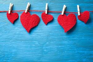 rojo corazones colgando en un hilo con pinzas para la ropa en un ligero azul antecedentes. foto