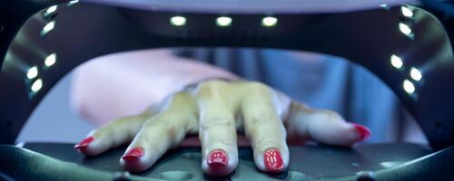 Photo showing the interior of an ultraviolet nail drying cabinet with a young woman's hand inside.