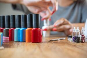 Colored nail polishes with a background of a woman painting her nails on a table with many accessories for work. photo