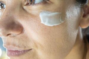 Skincare portrait. A young woman spread hydration cream on her face. Close up portrait of female care. photo