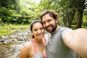 Hispanic couple takes a selfie in a river in Cordoba, Argentina, they are on vacation enjoying the stream. photo