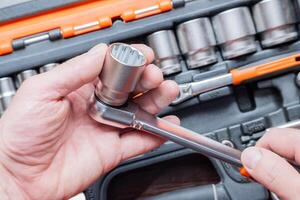 Hands of a man holding a ratchet wrench in the background you can see the toolbox. photo