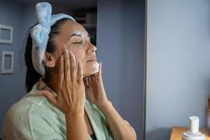Hispano mujer limpieza su cara a noche en frente de el vanidad. foto