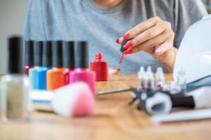 Woman paints her nails at the table at home. She has many nail polish colors to choose from. photo