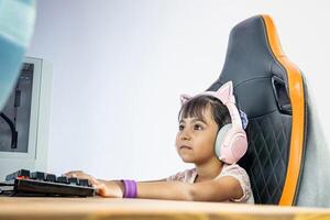 Girl in front of a gamer computer. She wears pink headphones with cat ears. She stares at the monitor. photo