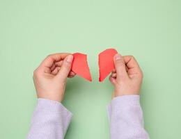 Two female hands tearing a red paper heart, symbolizing divorce photo