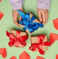 Woman's hand holding a gift box wrapped in a red silk ribbon on a green background, top view photo