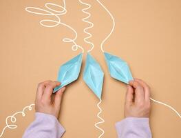 Three paper boats with different trajectories in a womans hand on a brown background photo