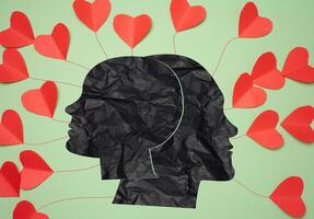 Silhouettes of a male and female head in the middle of red paper hearts photo