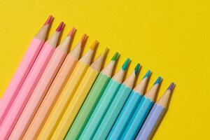 Multi-colored wooden pencils on a yellow background, top view photo