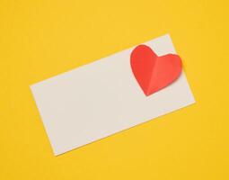 Rectangular white paper envelope and red heart on a yellow background photo