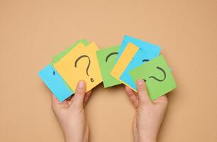 Female hands hold paper sheets with a drawn question mark on a beige background photo