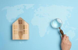 Wooden house on a world map background with a person's hand holding a magnifying glass photo