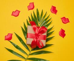 Gift box with red satin ribbon and bow on a yellow background. photo