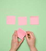 Pasted pink blank square paper stickers on green background photo