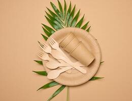 Paper plates and cups, wooden spoons and forks on a beige background photo