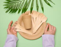 Paper plates and cups, wooden spoons and forks on a green background photo