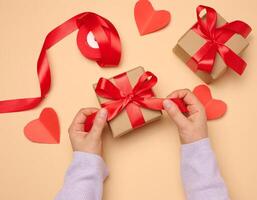 A woman's hand holds a gift box wrapped in a red silk ribbon on a beige background photo