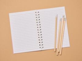 Open notebook and wooden pencils on brown background photo