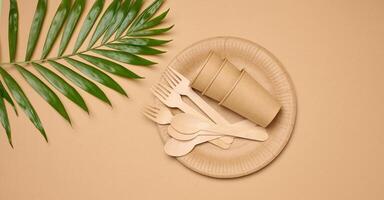 Paper plates and cups, wooden spoons and forks on a beige background photo