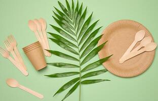 Paper plates and cups, wooden spoons and forks on a green background photo