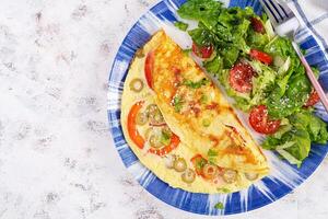 Omelette with tomatoes, green olives and fresh salad on blue plate.  Frittata - italian omelet. Top view, flat lay photo