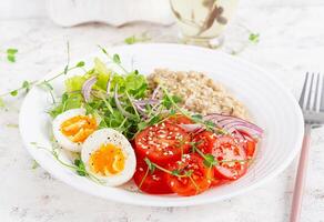 Breakfast oatmeal porridge with boiled eggs and fresh vegetables. Healthy balanced food. Trendy food. photo