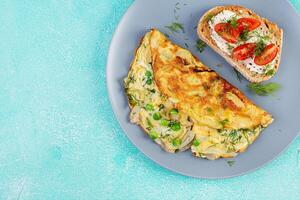 Omelette with green peas, onions and toast cream cheese, tomatoes on blue plate. Frittata - italian omelet. Top view, flat lay photo