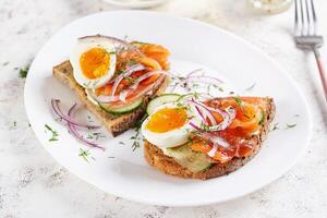 delicioso brindis con salmón, hervido huevo, Pepino y crema queso en un blanco lámina. sano comiendo, desayuno. ceto dieta alimento. sabroso alimento. foto