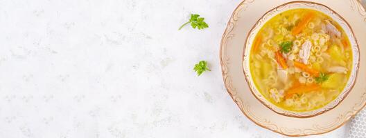Fresh chicken soup with vegetables and stelline pasta in a bowl with carrot and parsley. Top view, banner photo