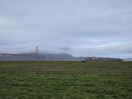 View of Golden Gate Bridge at a foggy day with a container barge passing by photo